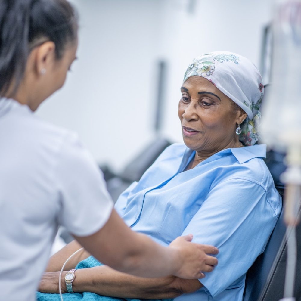 Oncology patient A woman wearing a head scarf recovers from chemo treatment in the hospital. A doctor speaks with her and offers her support.