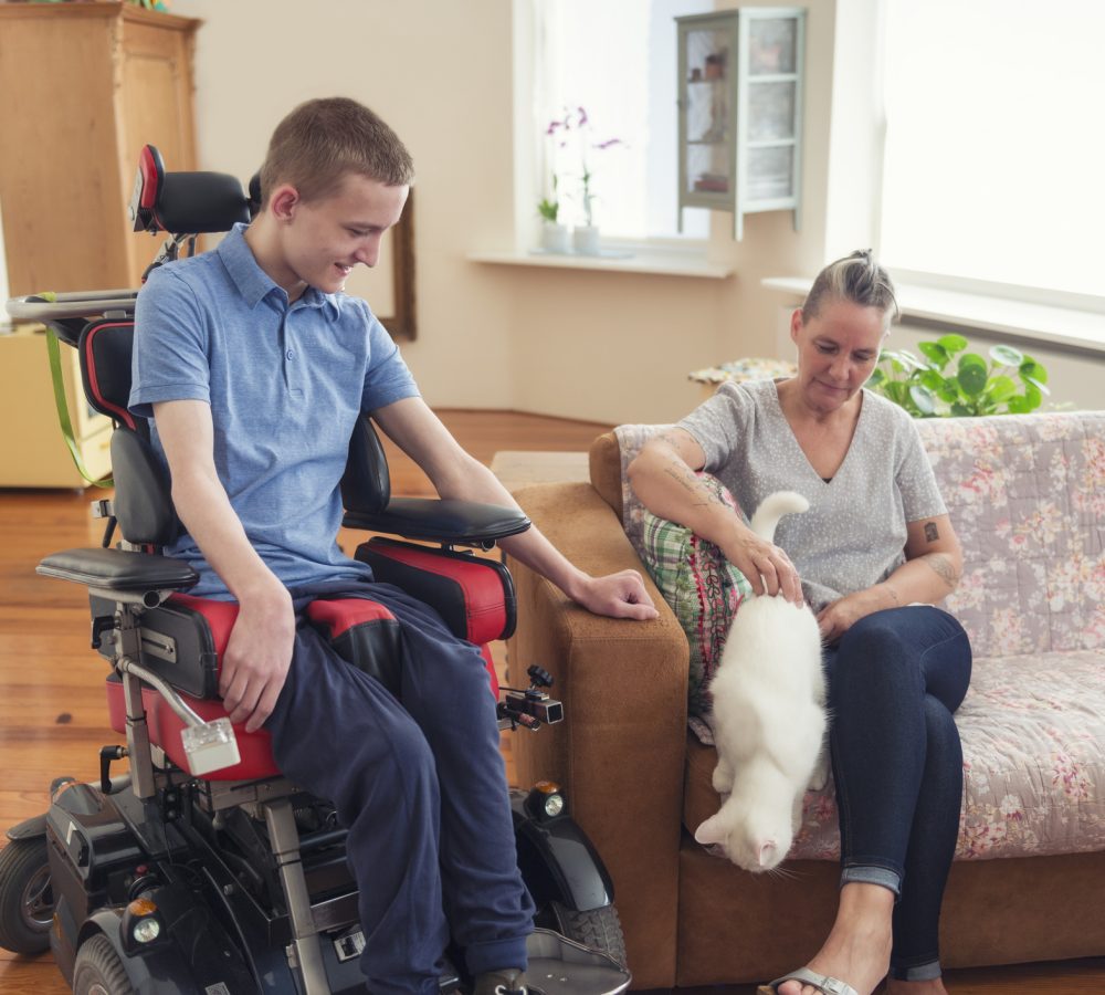 Happy day at home with disabled son Color image of a real life young physically impaired ALS patient spending time with his mother at home. They are happy.